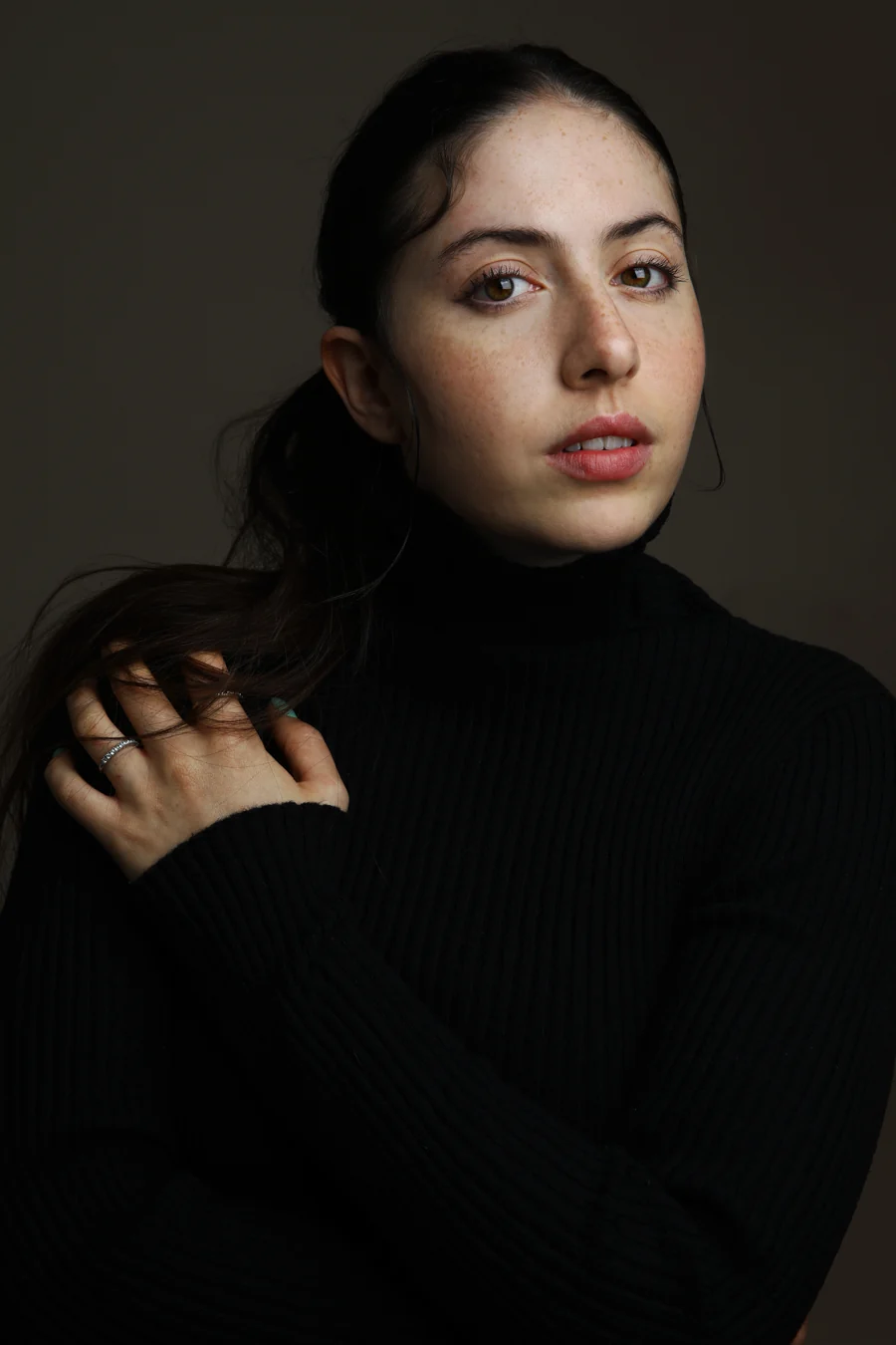 Theatrical headshot in a black ribbed turtleneck, hand at the collar